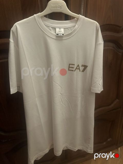 Ağ rəngli uniseks T‑şört. Ön hissədə qızılı “EA7” loqotipi, arxa — Bakı