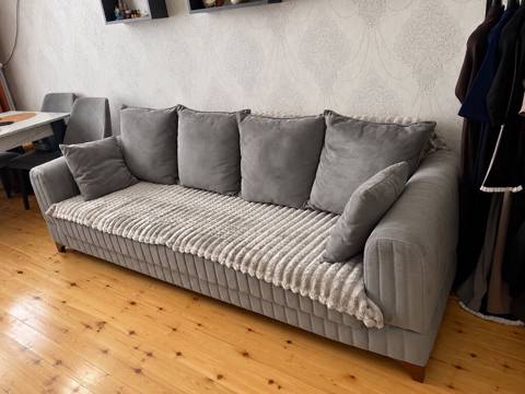 Boz rəngli, yumşaq toxumalı parça ilə örtülmüş geniş divan. - Üç — Xırdalan